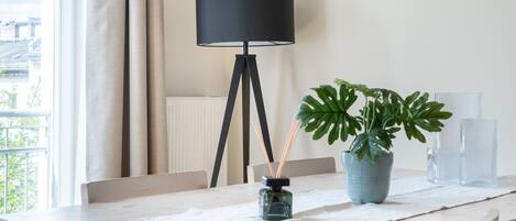 Une pièce moderne avec une table à manger en bois, une plante en pot, une lampe et une vue sur l’extérieur.