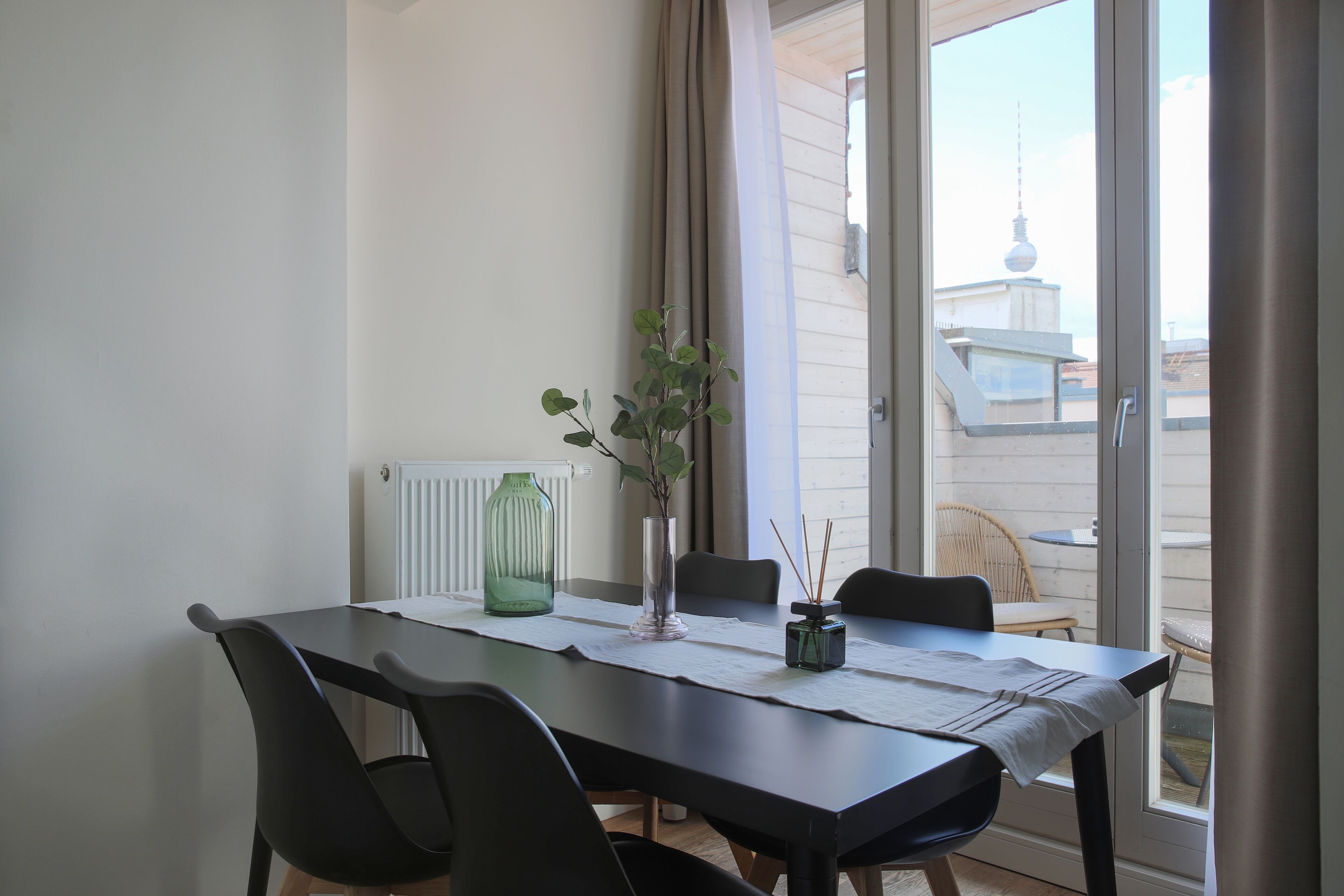 A dining area with a table, chairs, a vase with a plant, and a view of a building with a tower.
