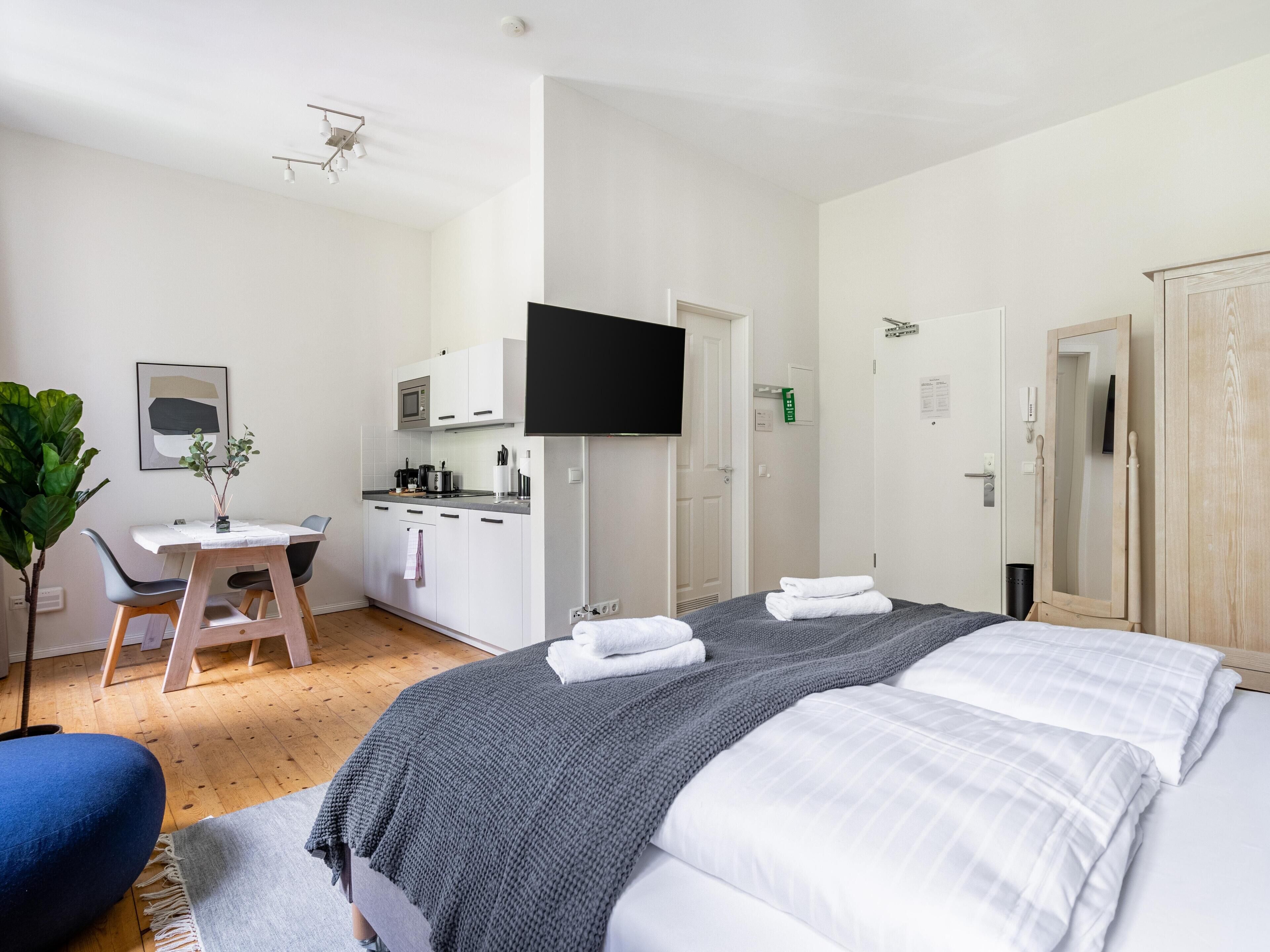 A modern hotel room with a large bed, a desk, and a kitchenette.