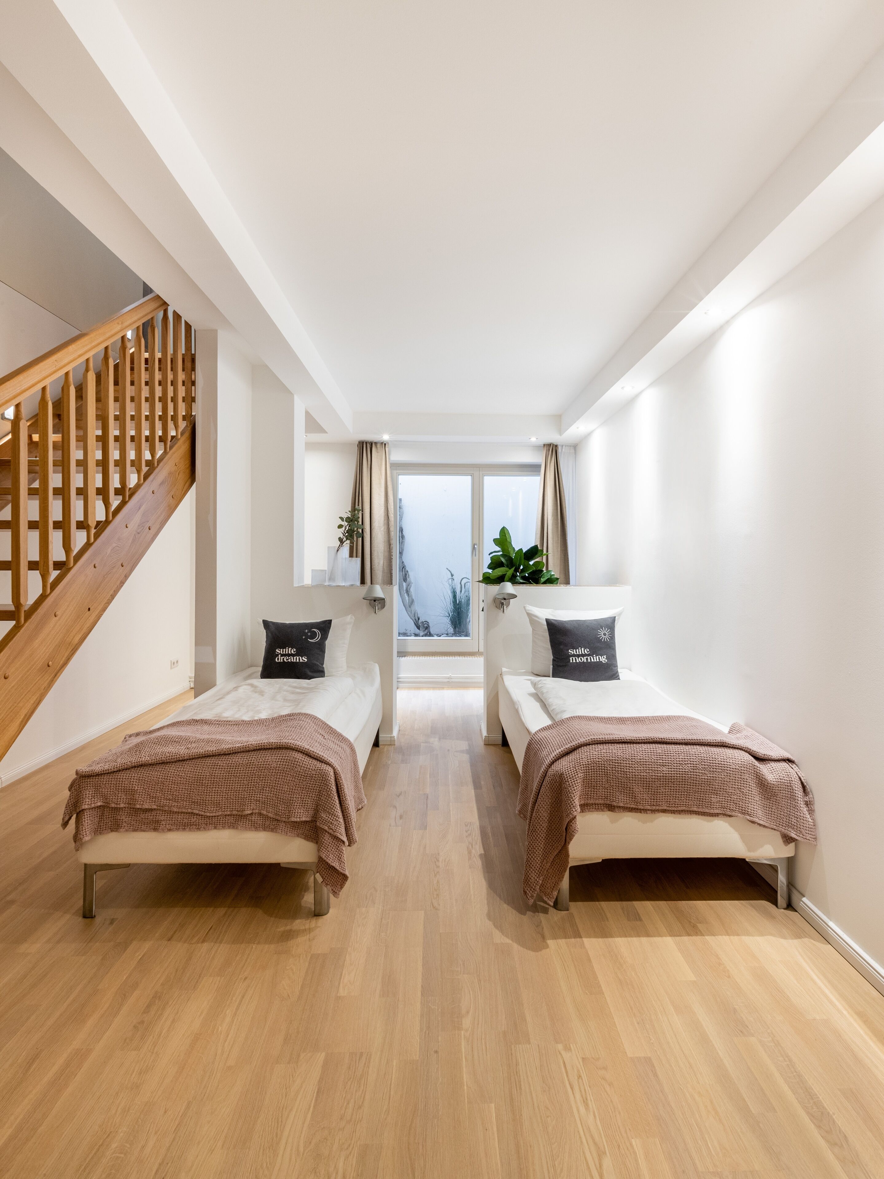 Une chambre d’hôtel moderne avec deux lits simples, un escalier en bois et une grande fenêtre donnant sur un beau paysage.
