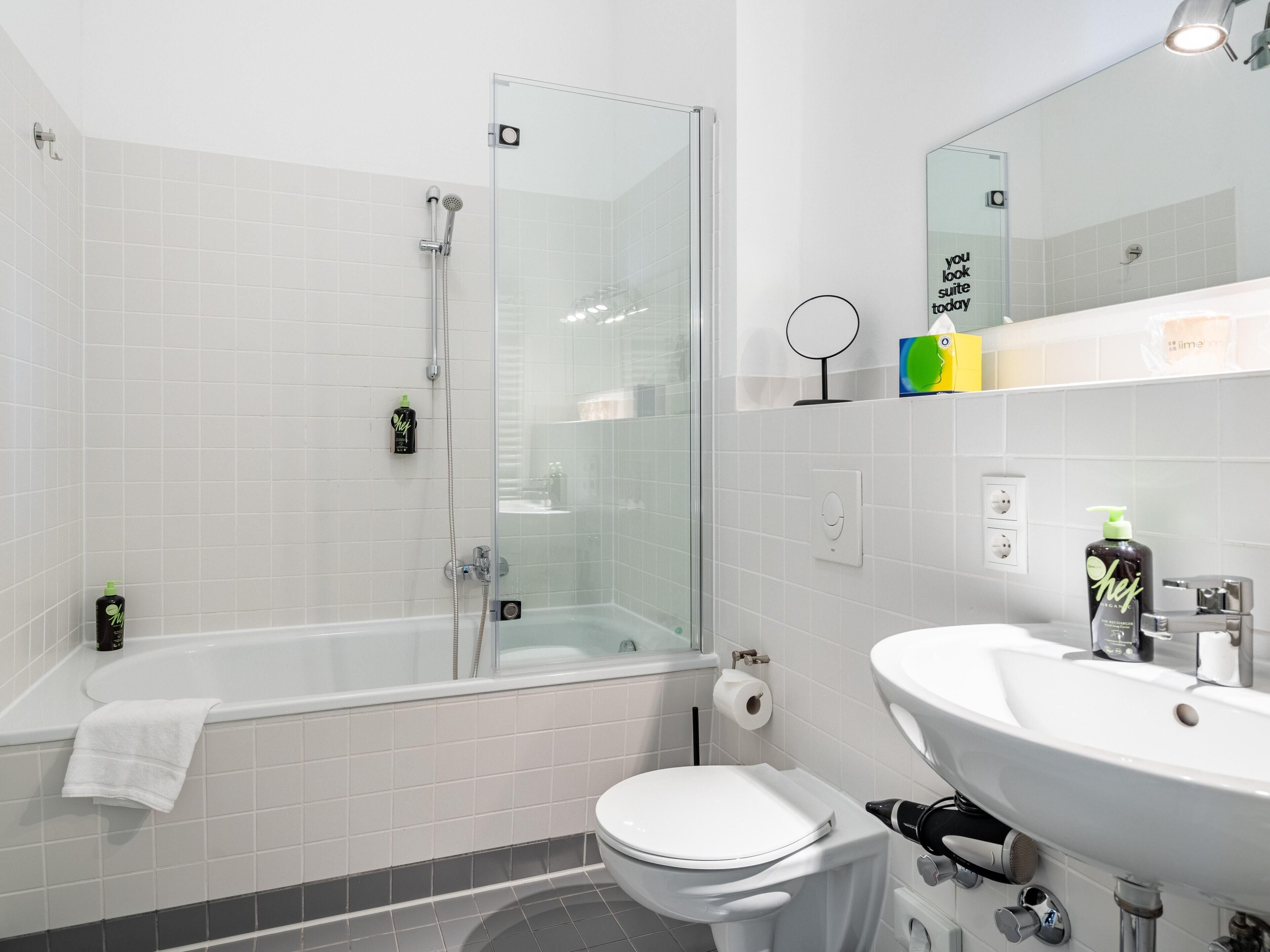 A modern bathroom with a glass-enclosed shower, a white toilet, and a sink with a mirror above it.