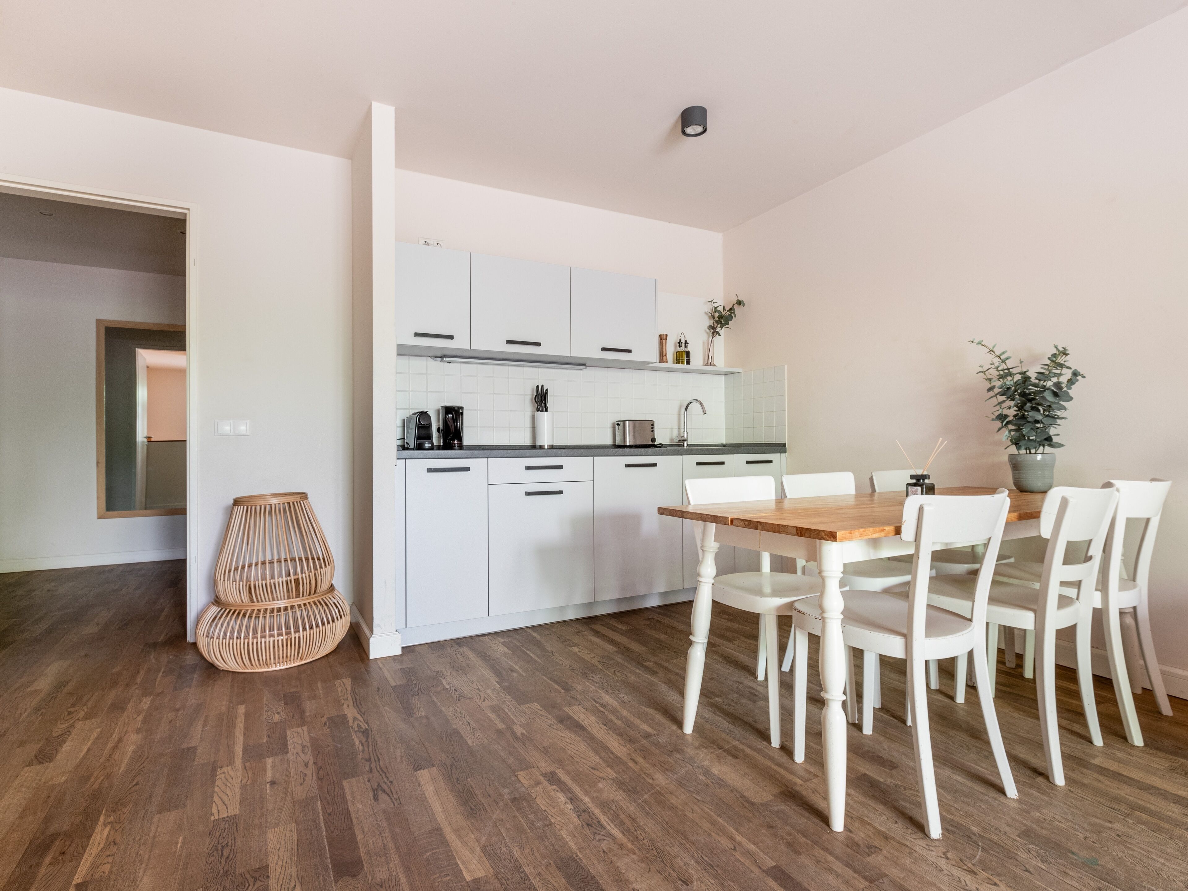 A modern kitchen with white cabinets, a wooden dining table, and white chairs.