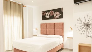 A modern bedroom with a large bed, a headboard, a wall-mounted TV, and a decorative wall piece. - Apartamentos Kouohana (Fuengirola)