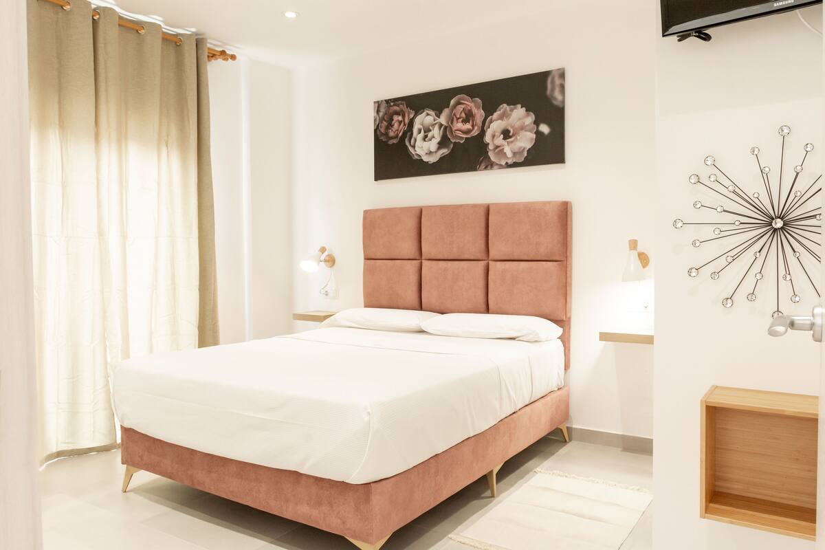 A modern bedroom with a large bed, a headboard, a wall-mounted TV, and a decorative wall piece.