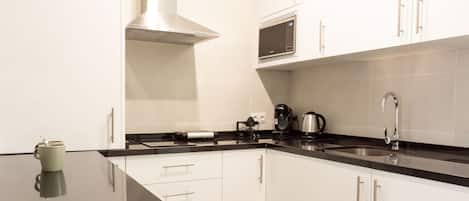 A modern kitchen with white cabinets, a black countertop, a stainless steel range hood, a microwave, a coffee maker, and a kettle.