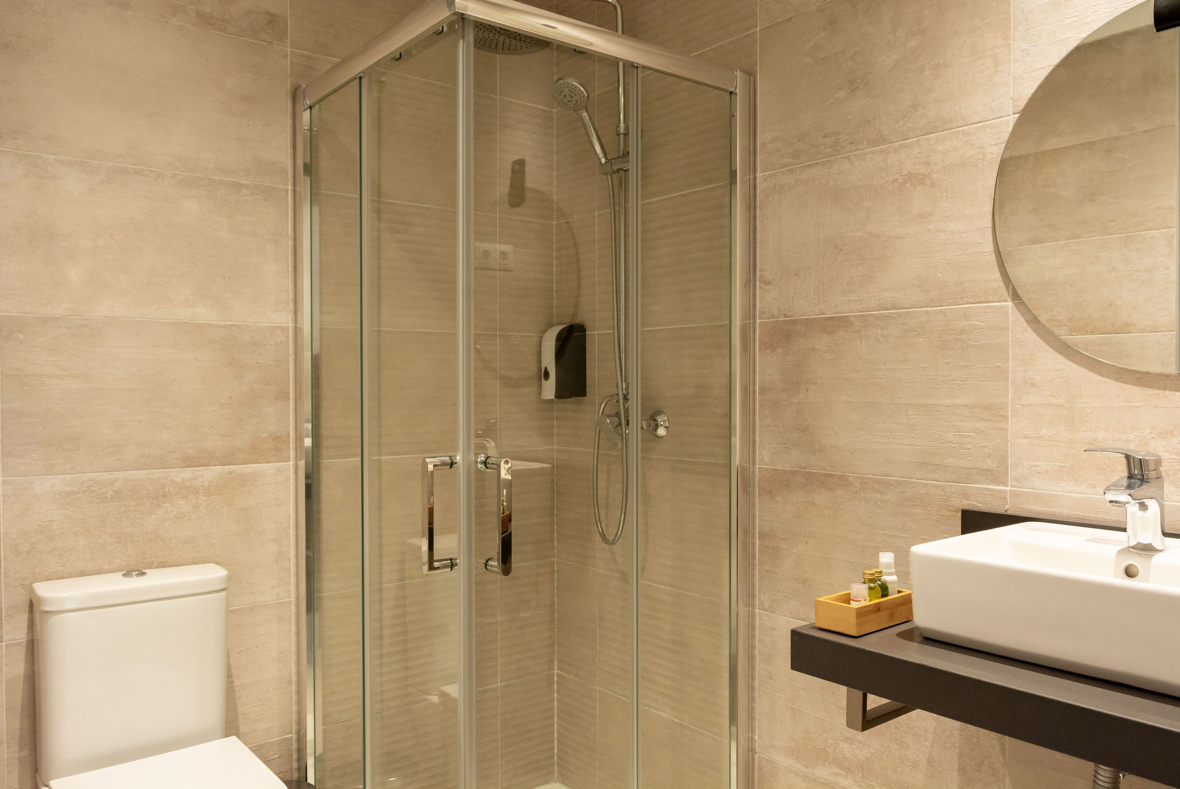 A modern bathroom with a glass-enclosed shower, a white toilet, and a sink with a wooden tray.
