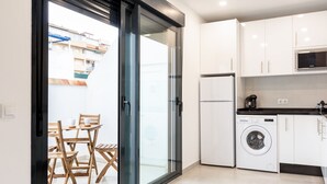 A modern kitchen with white cabinets, a washing machine, and a dining area with wooden chairs and a table. - Apartamentos Kouohana (Fuengirola)