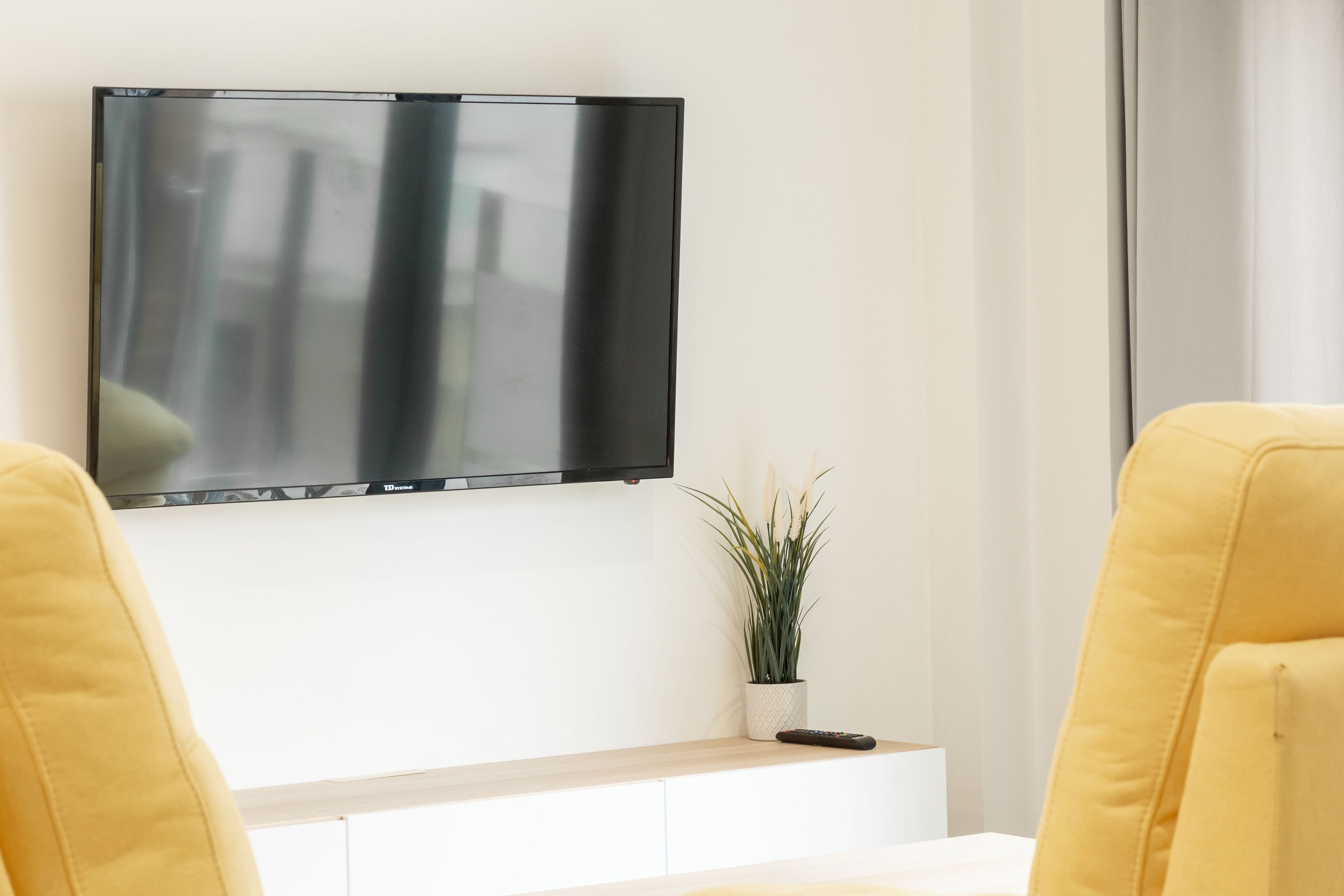 A modern living room with a flat-screen TV mounted on a white wall, a small potted plant, and a white console table.