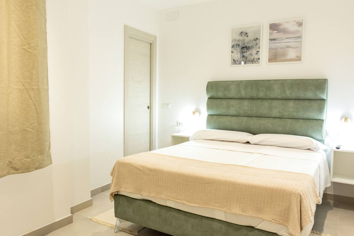 A bedroom with a green upholstered bed, white bedding, and two wall-mounted lamps.