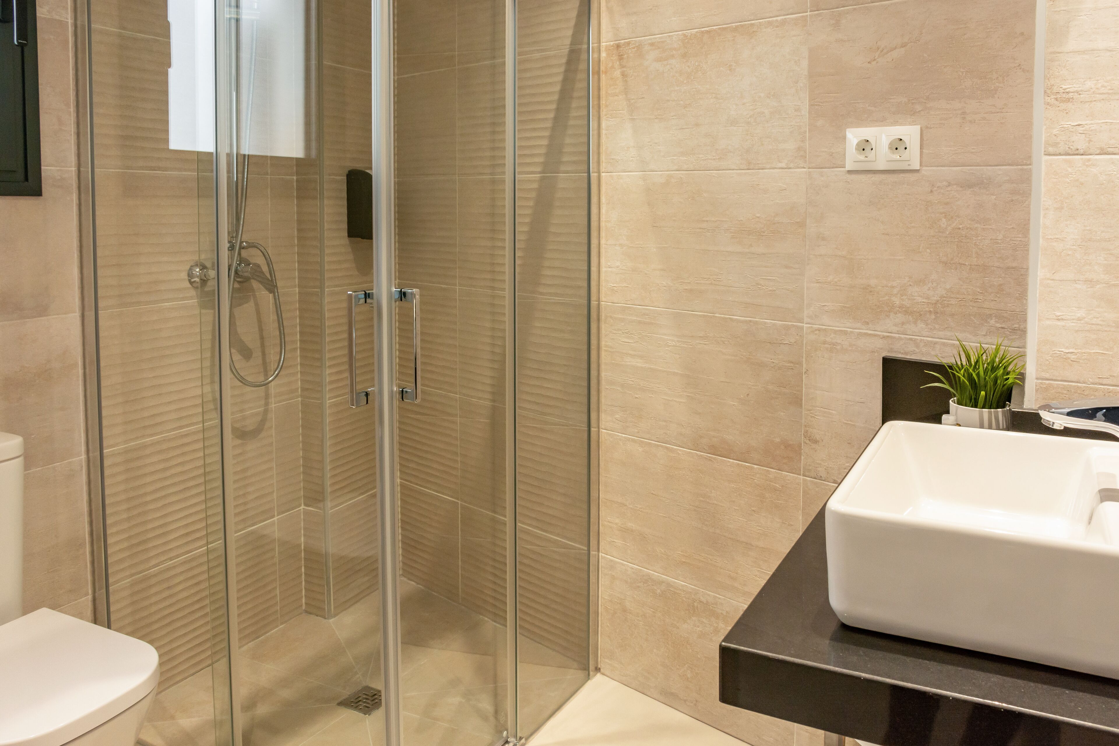 A modern bathroom with a glass-enclosed shower, a white sink, and beige tiles.