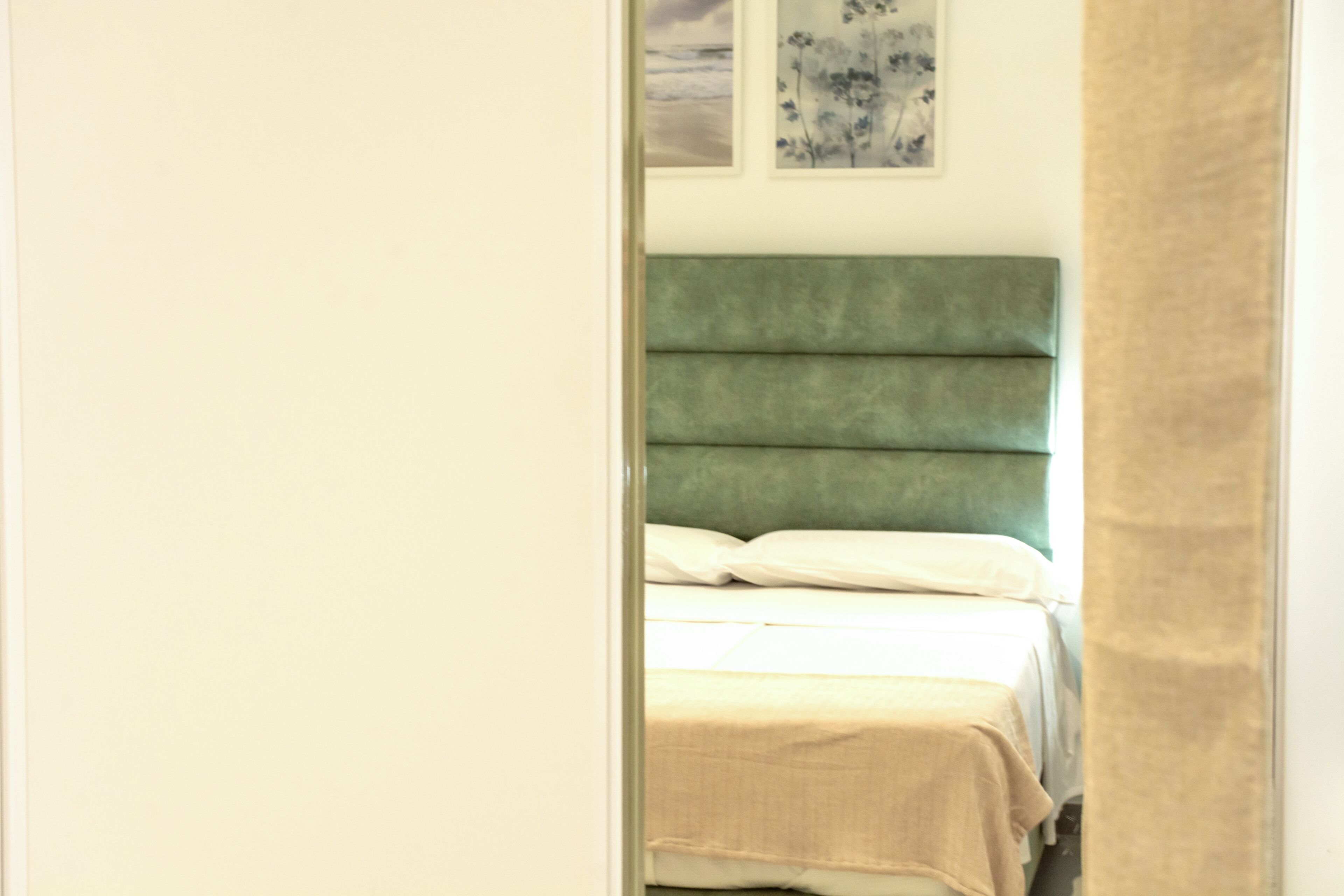 Un lit avec une tête de lit verte, une literie blanche et une couverture beige.