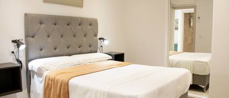 A bedroom with a large bed, two bedside tables, a wall-mounted lamp, and a painting above the bed.