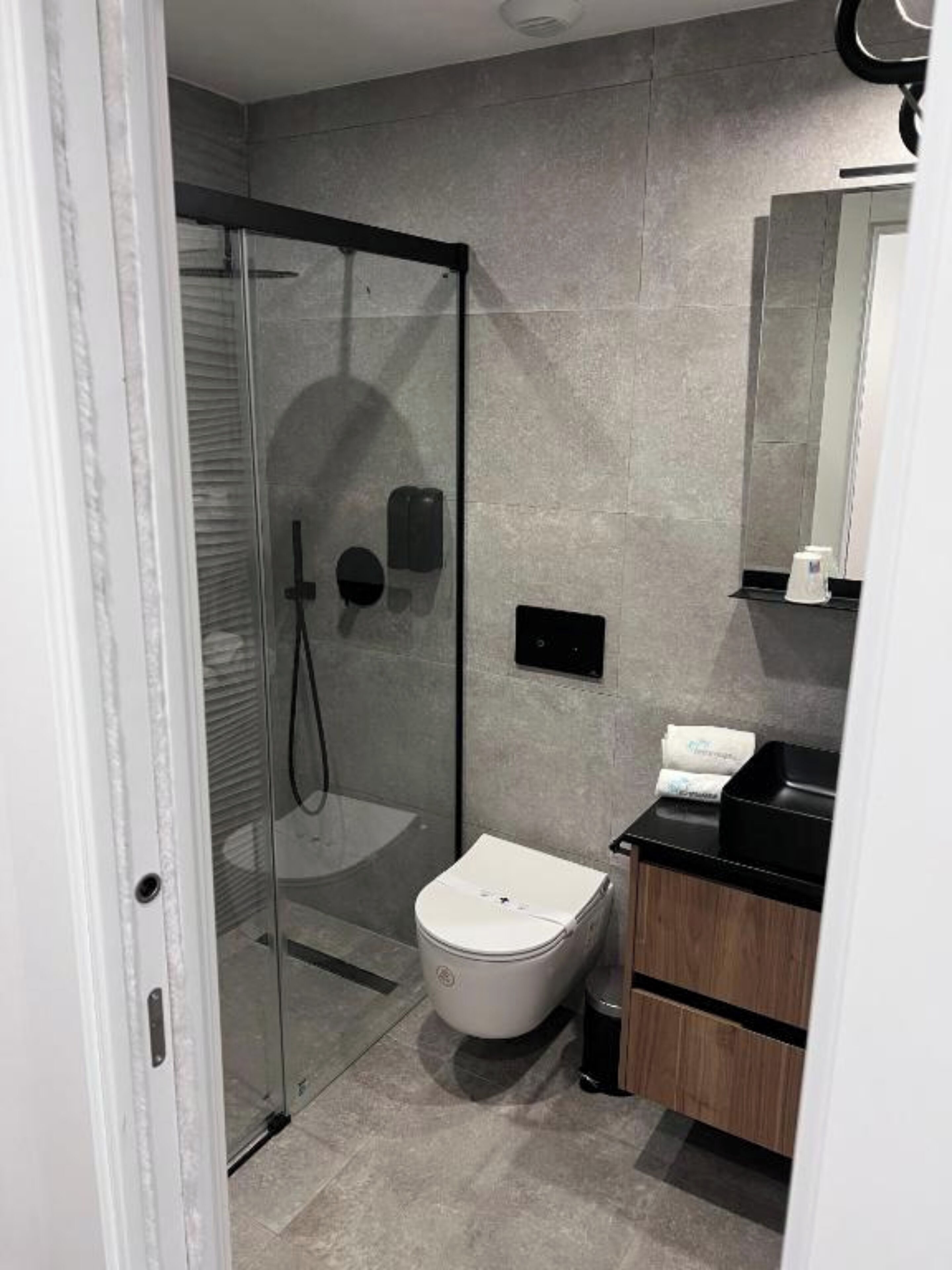 Et moderne badeværelse med en glasbrusekabine, et hvidt toilet og en trækommode med en sort bordplade.