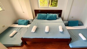 Et hotelværelse med en stor seng, to mindre senge og et vindue med udsigt til grønne omgivelser.