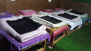Una fila de camas de madera con ropa de cama estampada, piso verde y pared marrón.