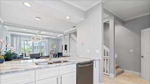 A modern kitchen with white cabinetry, a stainless steel dishwasher, and a marble countertop. - Pet-Friendly Cedars East Unit 847 by RVA (Longboat Key)