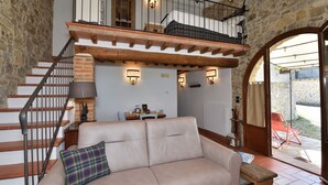 A cozy living room with a sofa, a dining table with chairs, a staircase, and a view of the outside. - Antica Posta, Castellina in Chianti, Siena and Chianti (Castellina in Chianti)