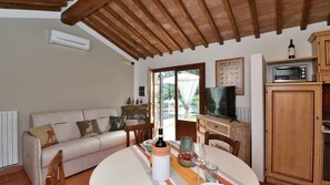 A cozy living room with a sofa, a dining table with a bottle of wine, a TV, and a cabinet.