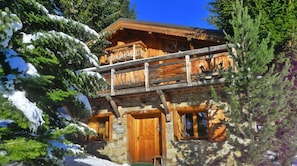 A chalet-style building with a wooden balcony, stone walls, and a wooden door.