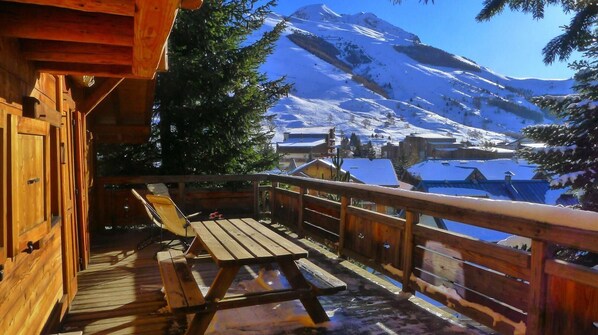 A wooden deck with a table and chairs, overlooking a snowy mountain landscape.