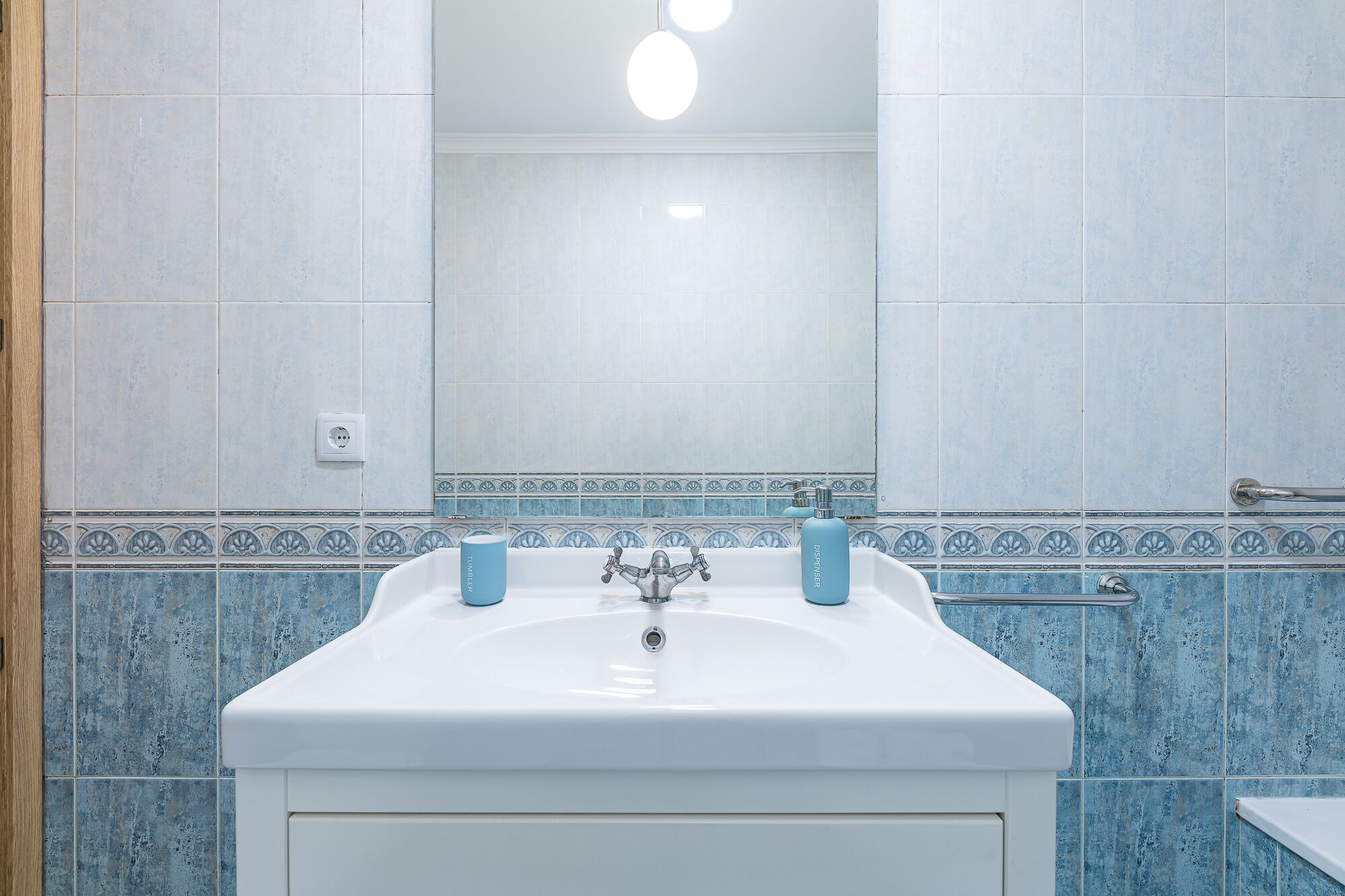 A bathroom with a white sink, two blue soap dispensers, a mirror, and blue patterned tiles.