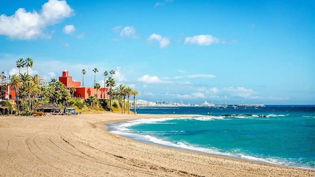 A beach with a building that has a red roof and palm trees. - Cozy townhouse in Benalmadena 3min from the beach (Benalmádena)