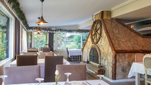 Un restaurante con chimenea de piedra, techo blanco y amplios ventanales con vistas a la vegetación.