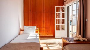 Een hotelkamer met een bed, een houten garderobe, een bureau met een lamp en een raam met gordijnen.