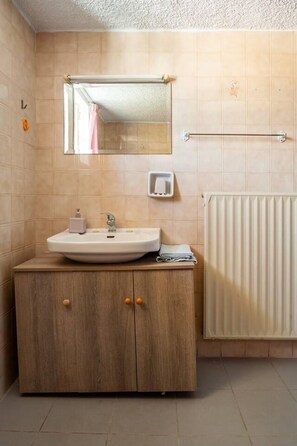 Een badkamer met een wastafel, spiegel, handdoekrek, zeepdispenser en radiator.
