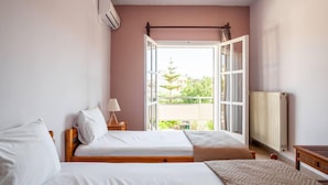 Een slaapkamer met twee bedden, een raam, een radiator en een nachtkastje met een lamp.