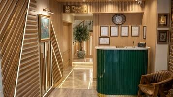 Um saguão de hotel com balcão de recepção, relógio, certificados emoldurados e um tapete estampado.