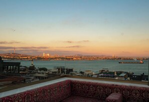 A cityscape view from a balcony with a patterned sofa, a ship in the water, and a distant city skyline. - By Kinyas Hotel (Istanbul)