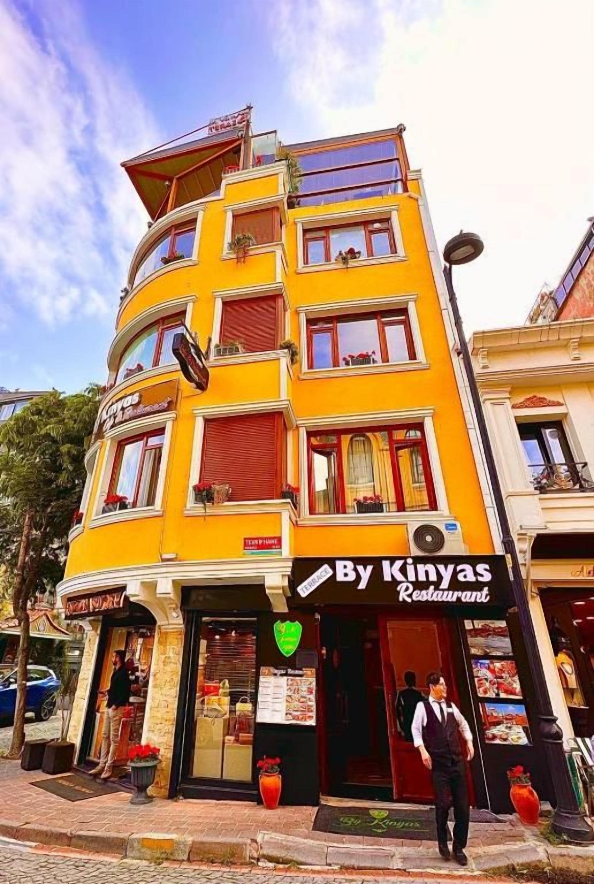 Um edifício de vários andares com um restaurante chamado 'By Kinyas Restaurant' no andar térreo.