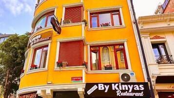 Um edifício de vários andares com um restaurante chamado 'By Kinyas Restaurant' no andar térreo.