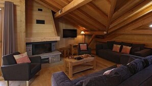 En hyggelig stue med trægulv, pejs, to sofaer, et sofabord og et tv ophængt på væggen.