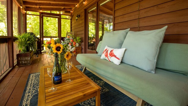Une terrasse en bois avec un canapé et une table sur laquelle se trouvent une bouteille et un verre.
