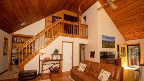 Un salon spacieux avec un escalier en bois, un canapé en cuir et une vue sur l’extérieur.