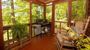 Une terrasse en bois avec un barbecue, un banc et une chaise berçante.