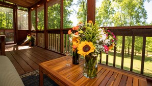 Une terrasse en bois avec une table, un vase de fleurs et une bouteille de vin.