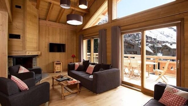 A cozy wooden interior with a fireplace, sofas, and a large sliding glass door to a deck.