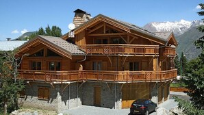 A wooden chalet with a balcony, stone foundation, and a car parked in front.