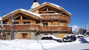 A multi-story wooden chalet with a balcony, surrounded by snow.