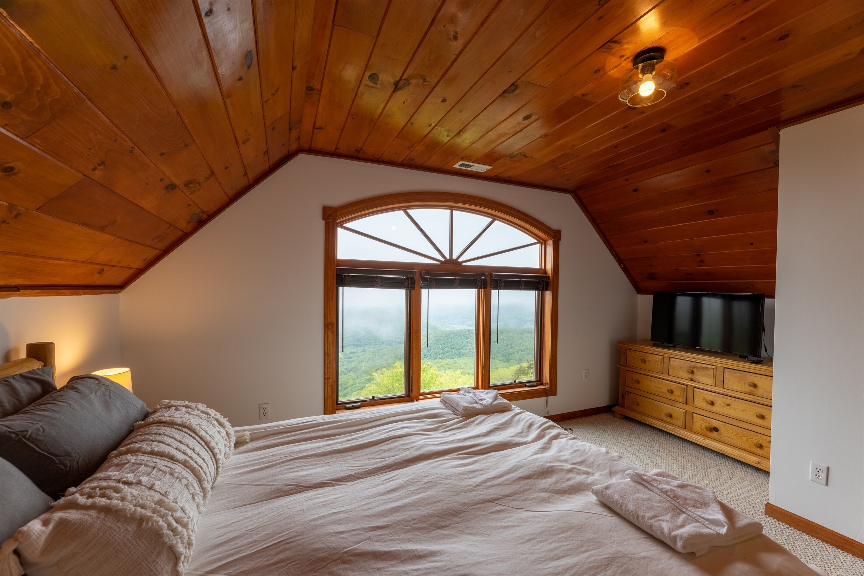 Ein Schlafzimmer mit einem großen Bogenfenster, Holzbalkendecke und einem Schminktisch.