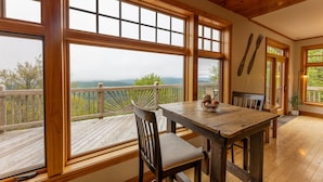 A wooden deck with a table and chairs, large windows, and a view of the mountains. - Gorgeous Chalet - Incredible Views - Hot Tub - Fire Pit (Snowshoe)