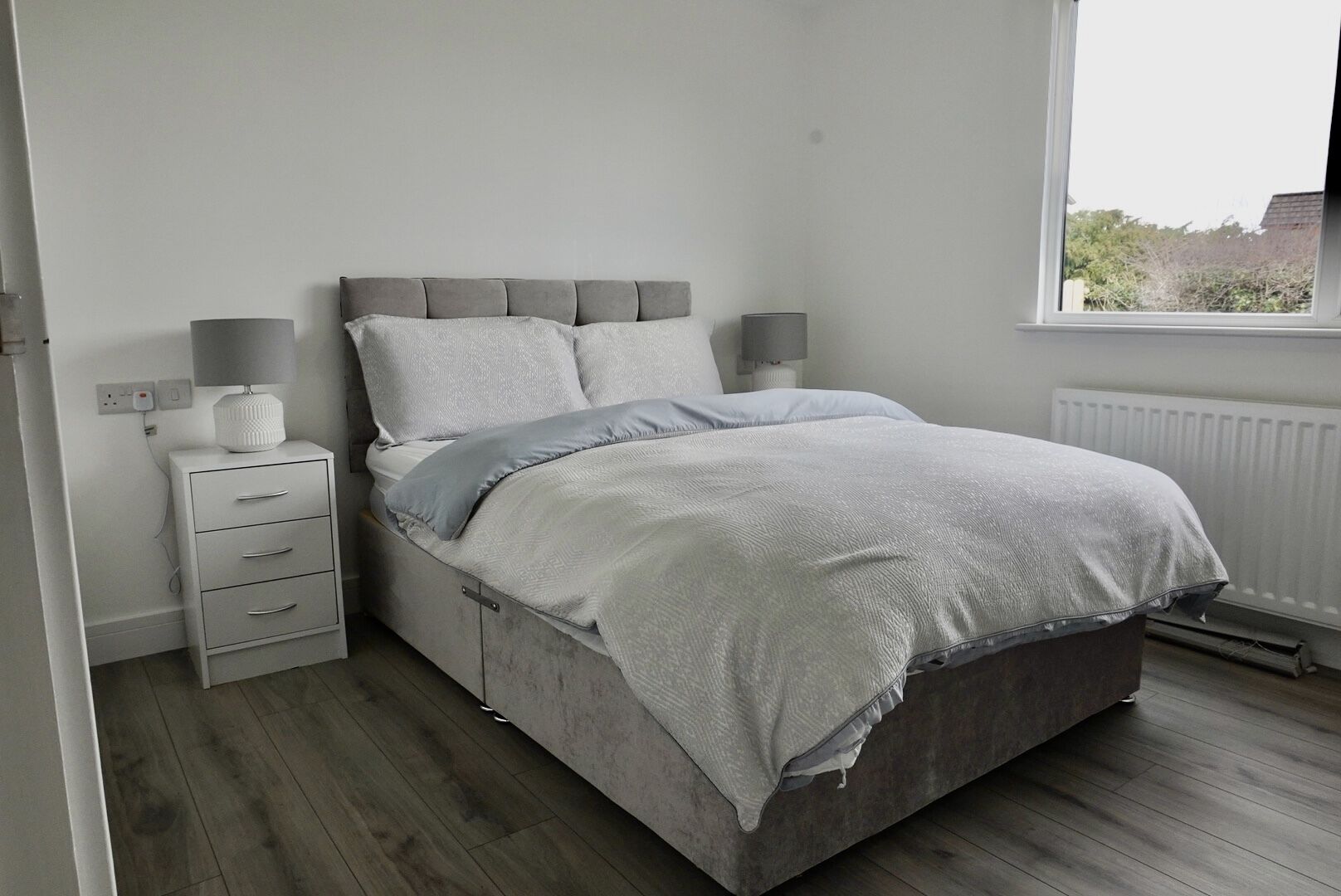 A bedroom with a bed, bedside lamps, a nightstand, and a window.