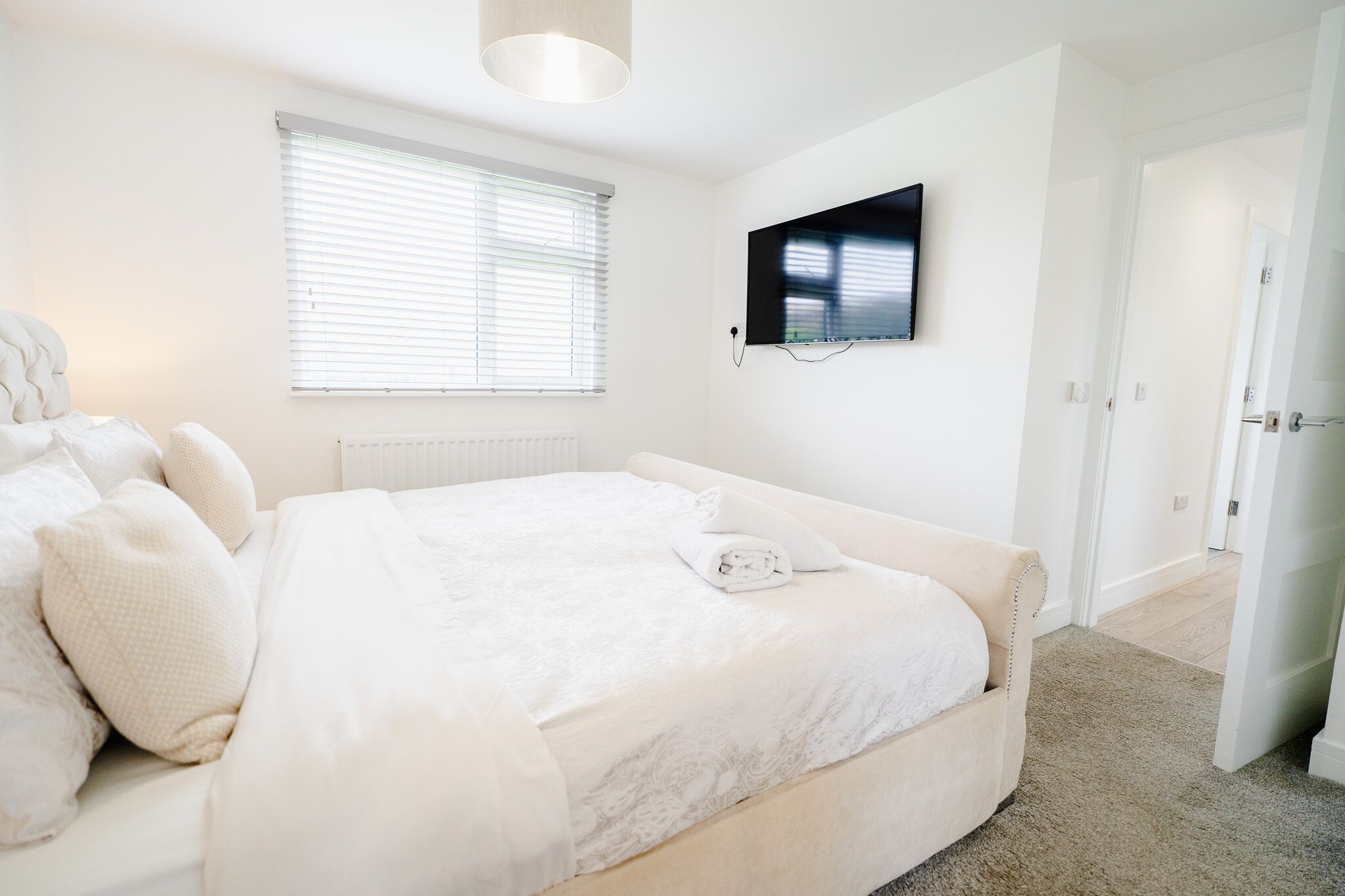 Un dormitorio con cama, televisor montado en la pared y ventana con persianas.