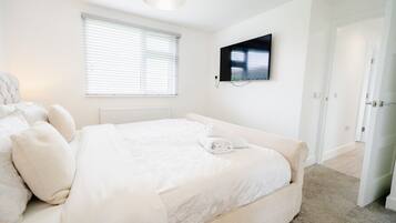 Un dormitorio con cama, televisor montado en la pared y ventana con persianas.