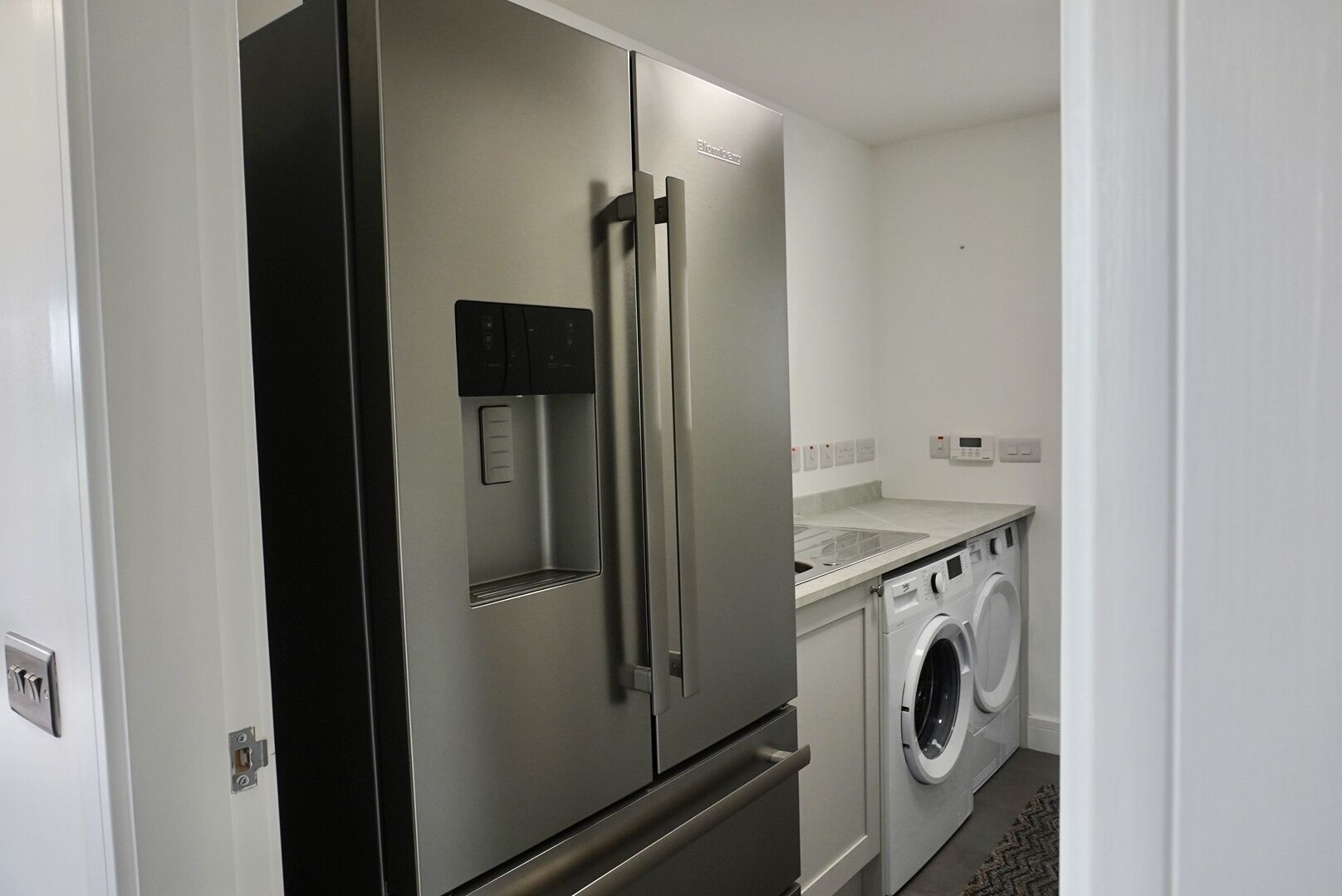 A compact kitchen with a stainless steel refrigerator, a built-in oven, a washing machine, and a sink.