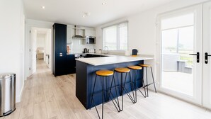 A modern kitchen with a central island, bar stools, and a large window. - Castle View Chalet by Clonlum Cottages (Newry)
