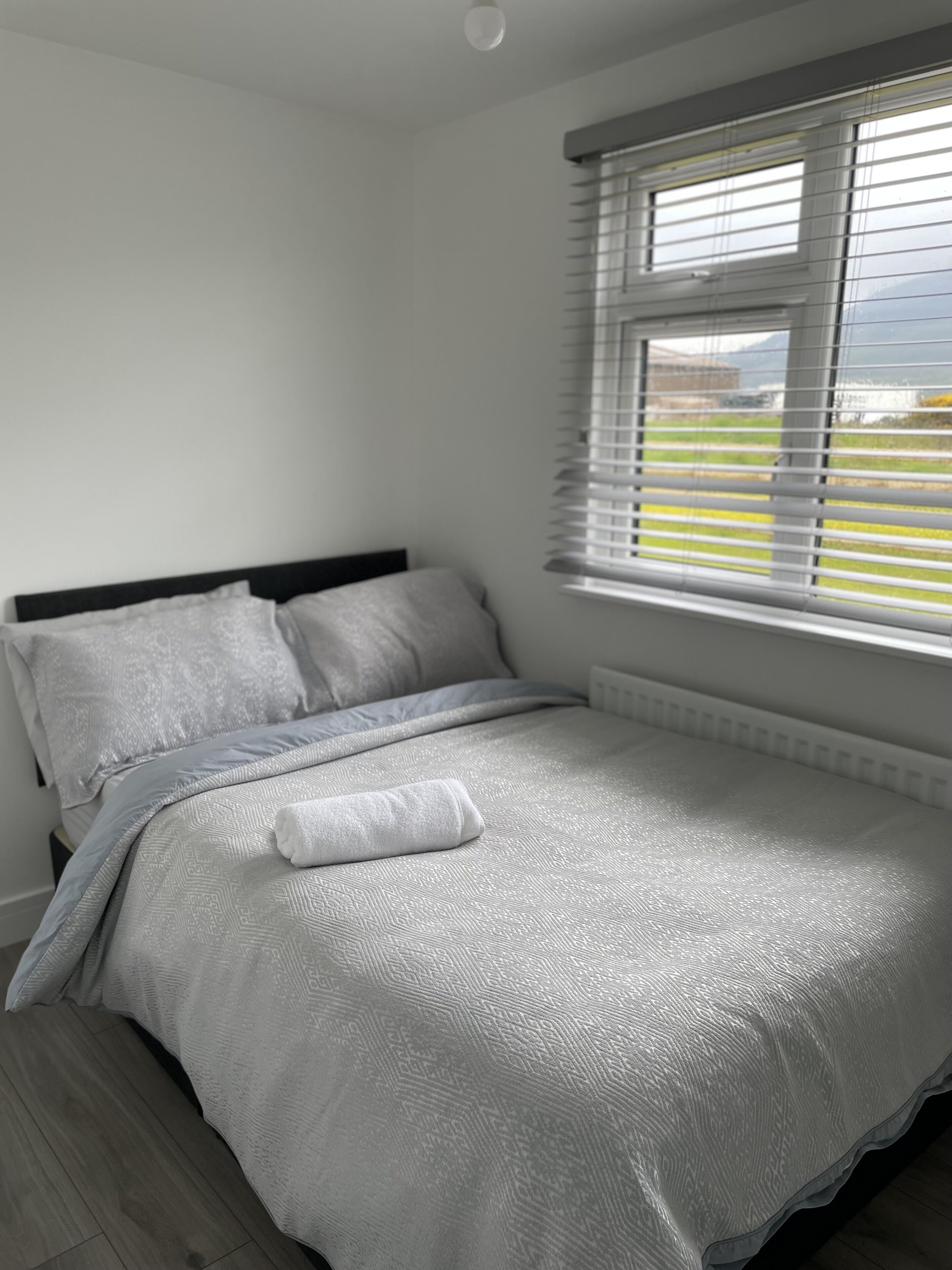 A bedroom with a bed, a window with blinds, and a view of greenery outside.